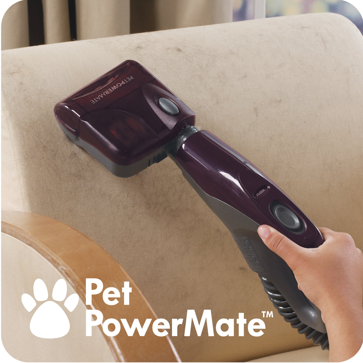 Hand using a Pet PowerMate vacuum cleaner attachment on a beige couch.