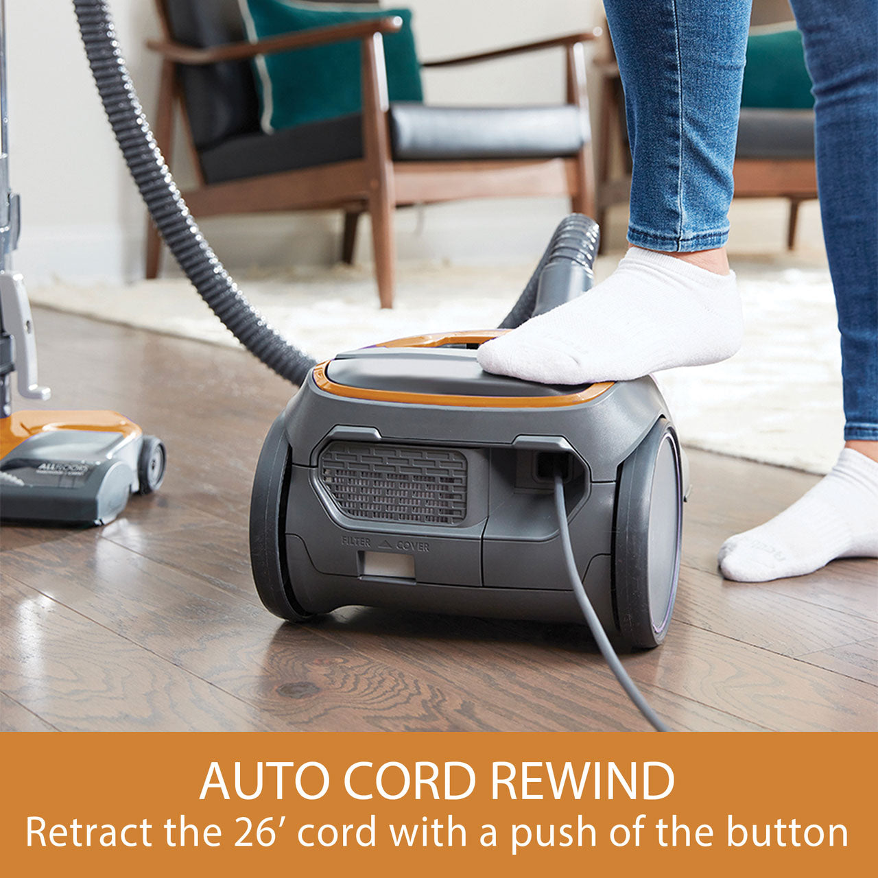Person using a canister vacuum cleaner with auto cord rewind feature on a wooden floor.