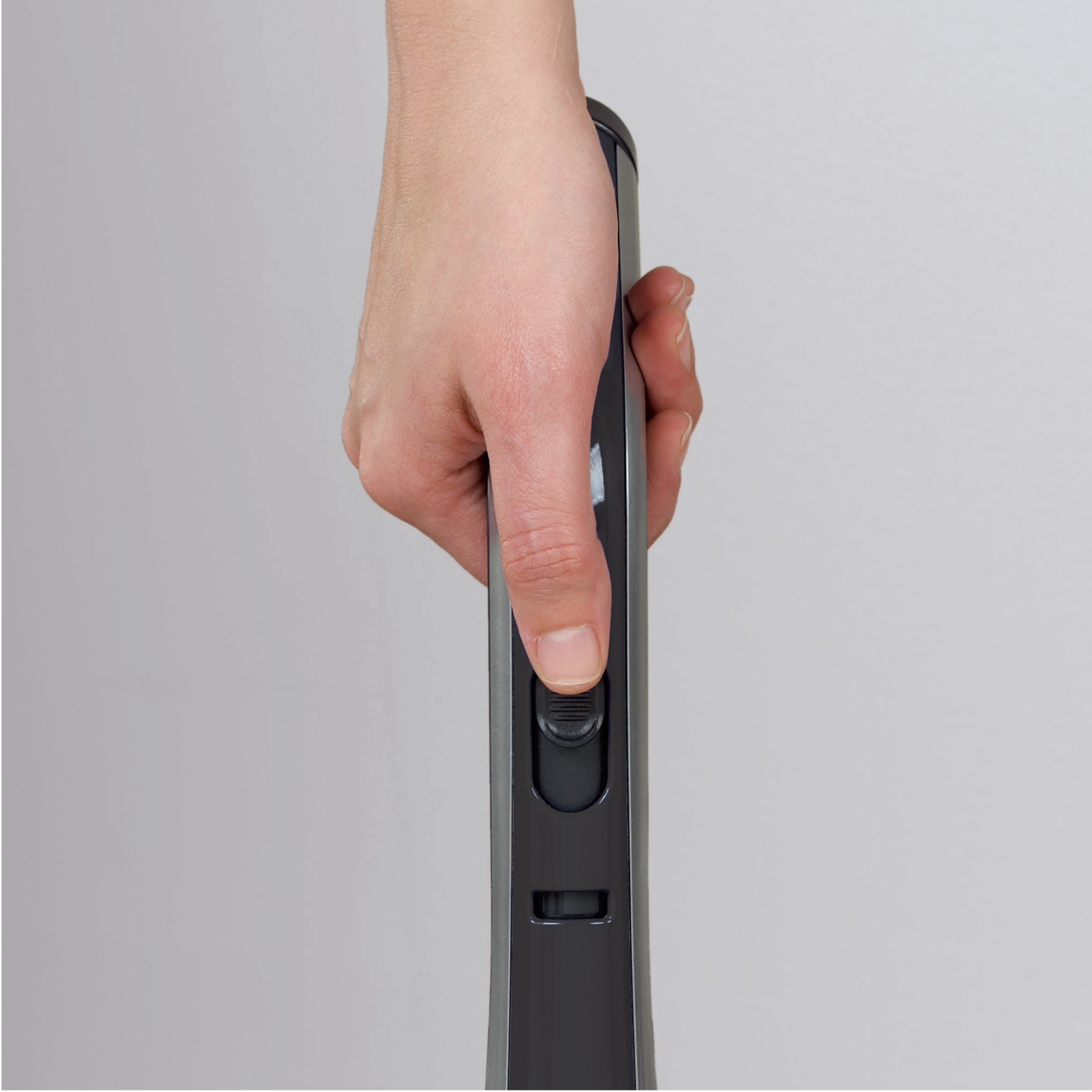Hand holding the controls of an upright vacuum on a gray background