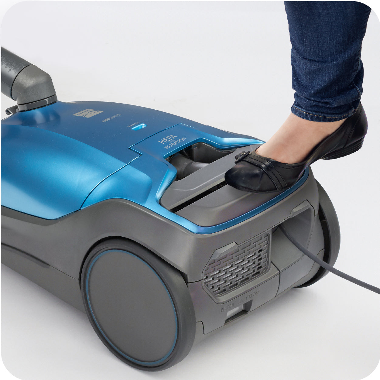 Person presses cord rewind button on back of a blue vacuum with foot.