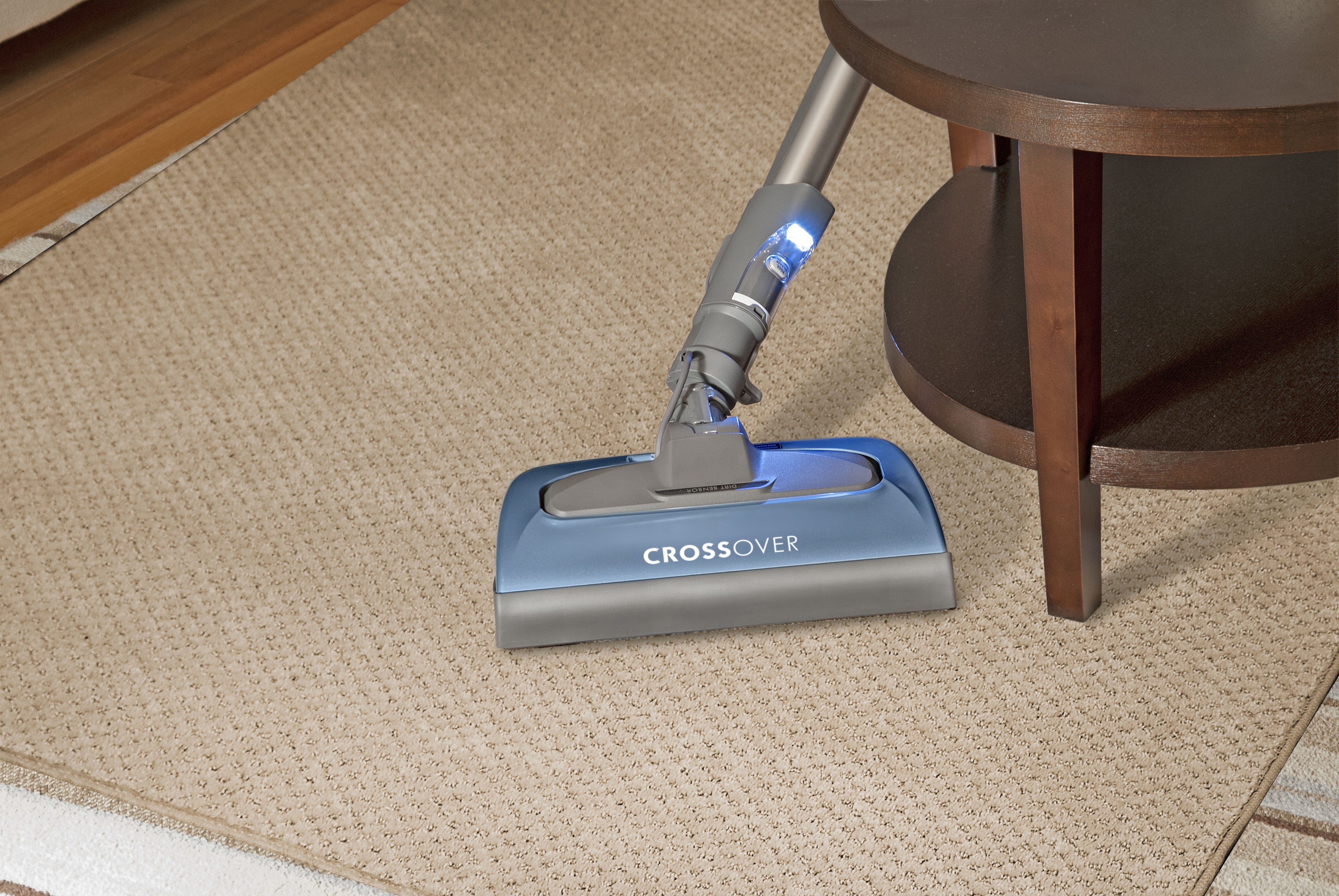 Vacuum nozzle with "Crossover" text on it swiveling around a table on carpet.