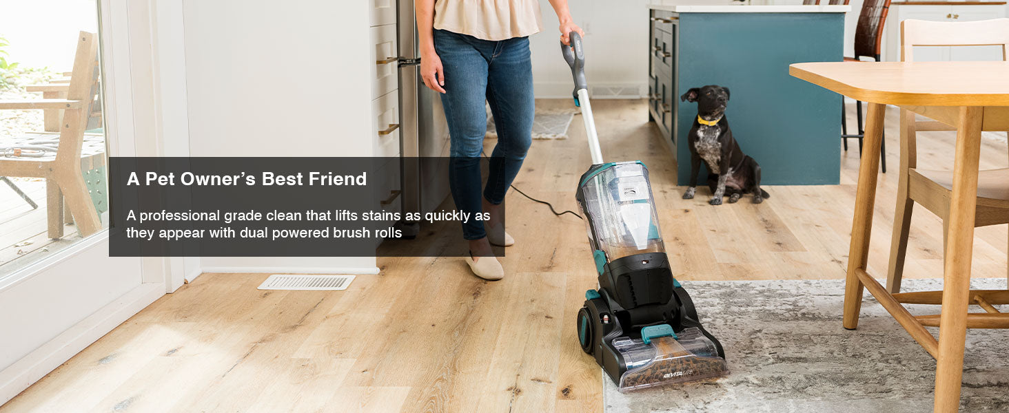 Woman using a carpet cleaner in a modern kitchen with a dog watching.