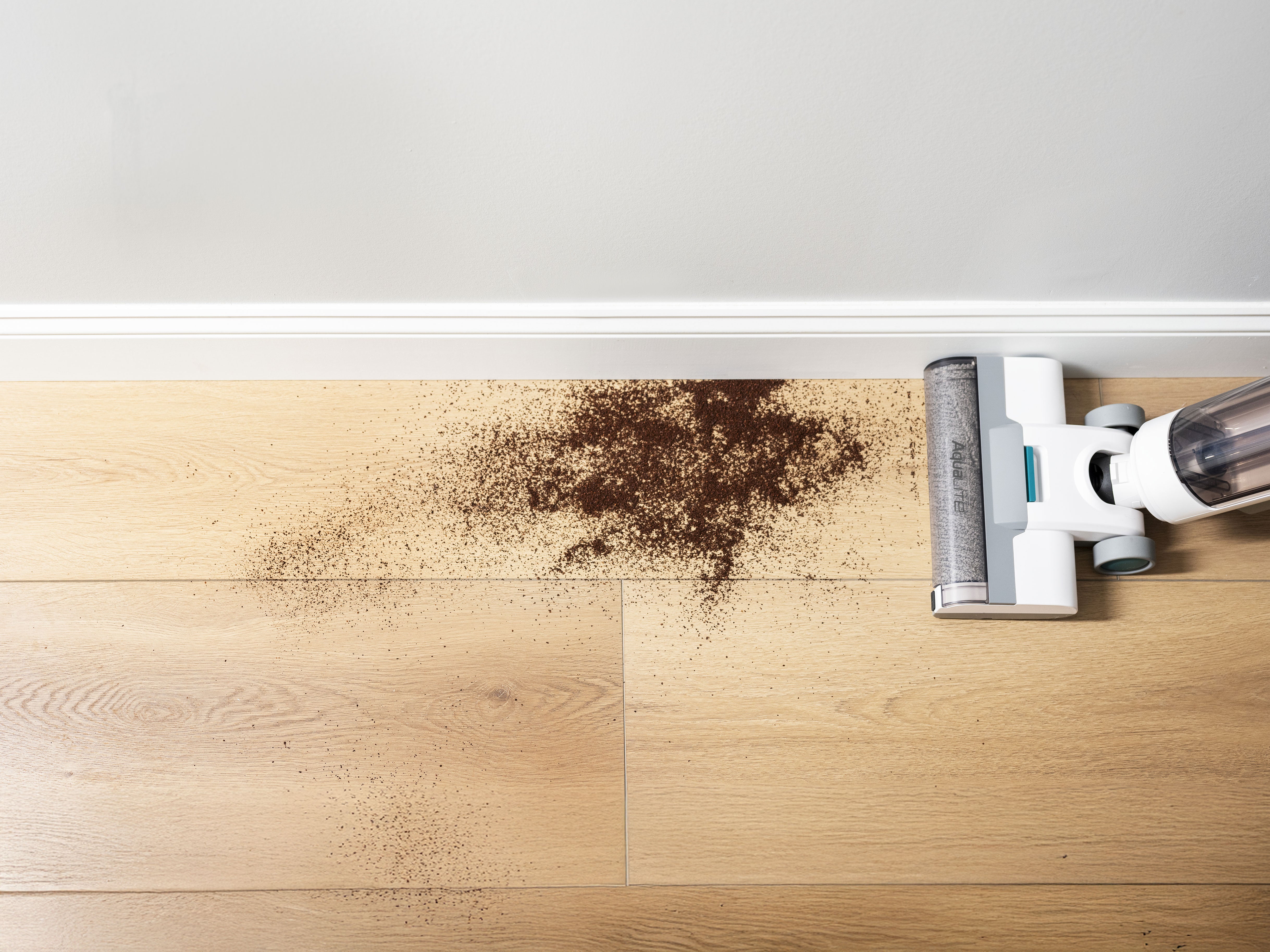 Vacuum cleaner cleaning a wooden floor with visible dirt being picked up from the edge of the wall.