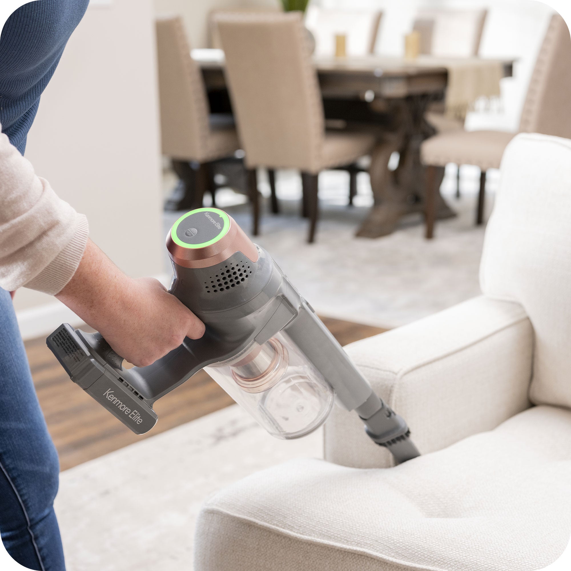 Person using a handheld vacuum cleaner on a white sofa in a living room.
