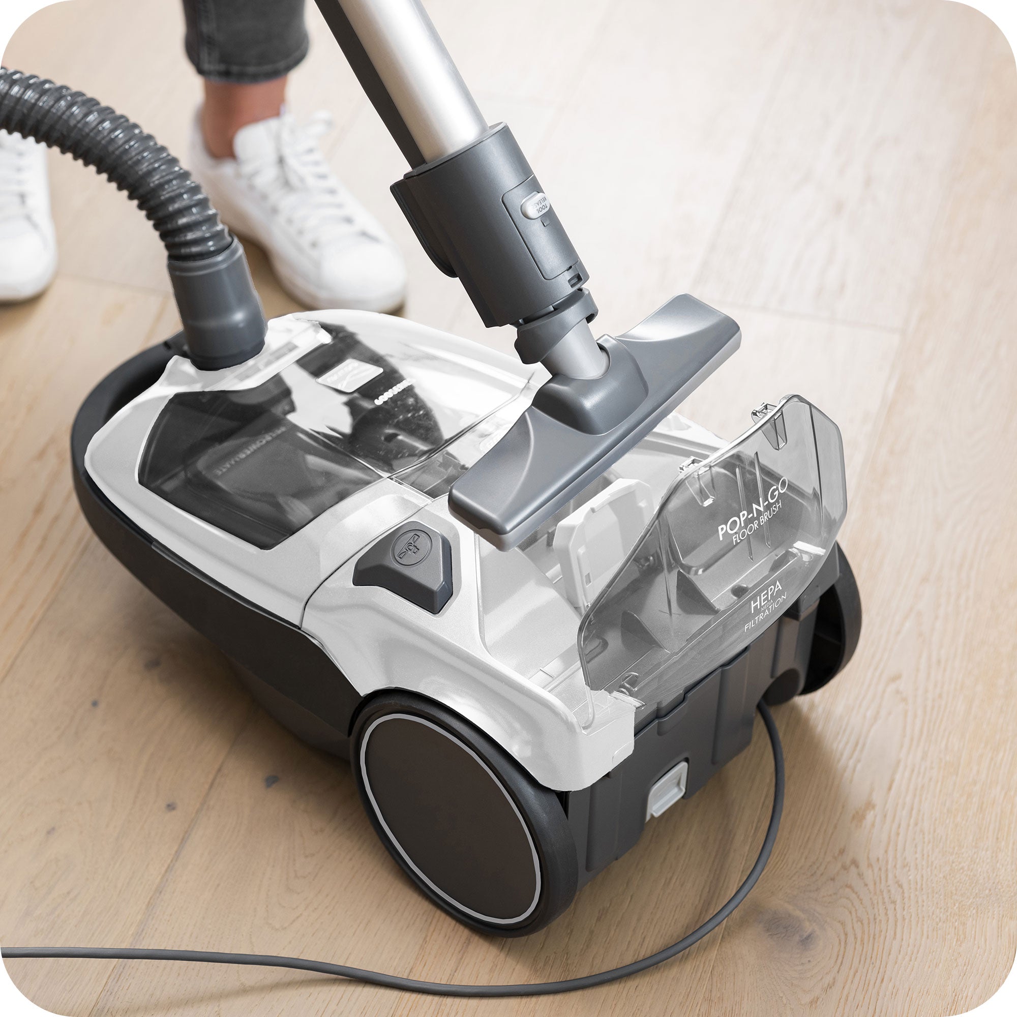 Canister vacuum cleaner illustrating the POP-N-GO feature on a wooden floor with a person cleaning.