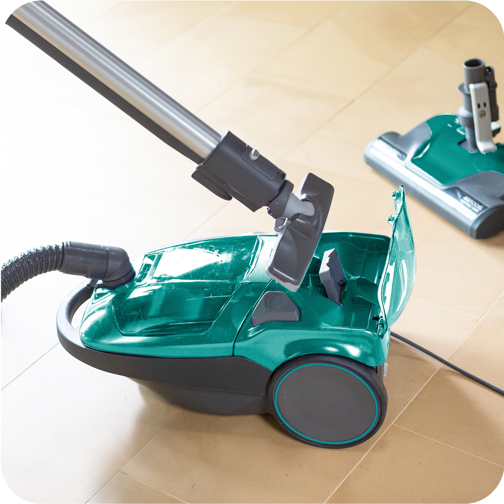 Green canister vacuum cleaner on a tiled floor illustrating POP-N-GO bare floor tool attachment