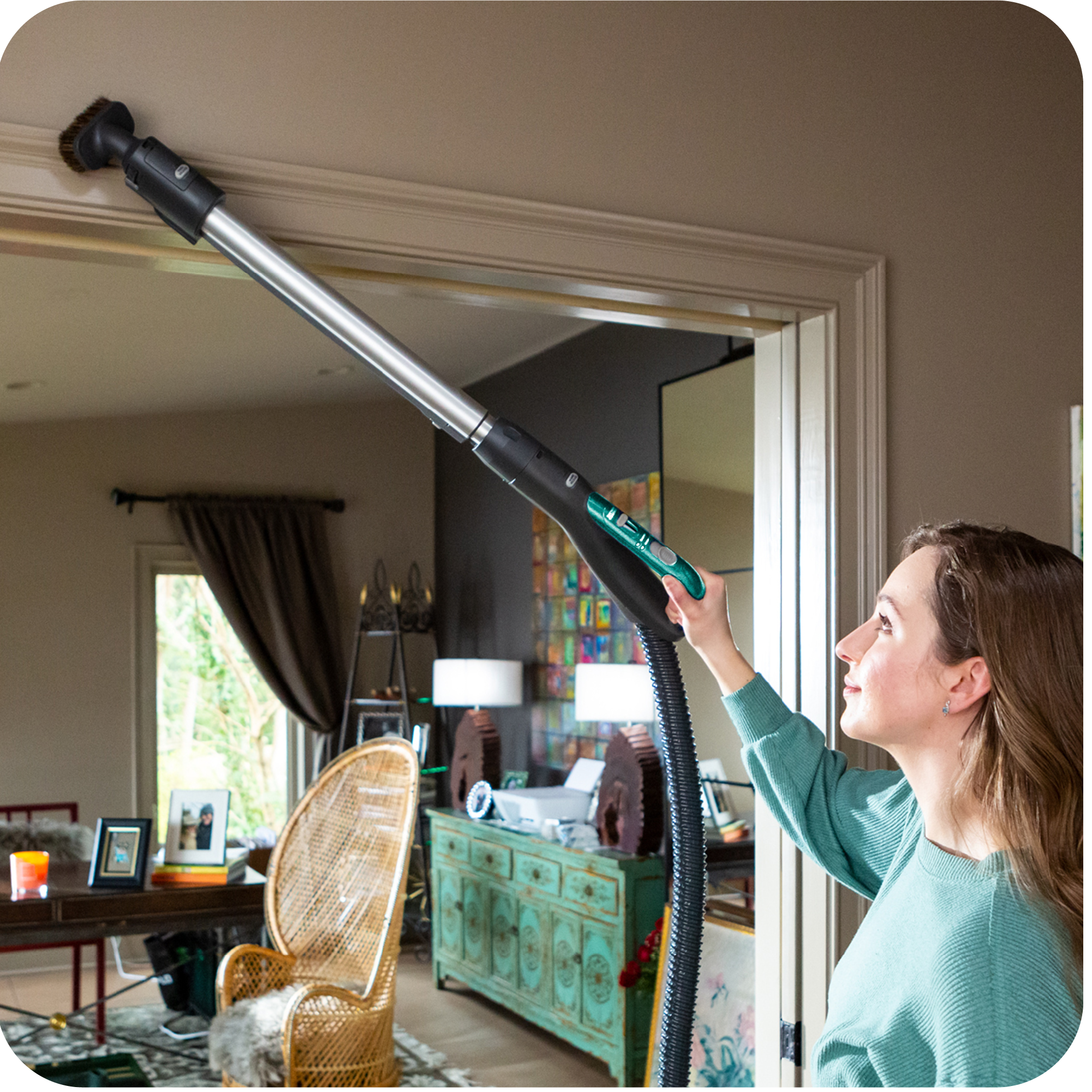 Woman cleaning a doorway with a canister vacuum in a living room.