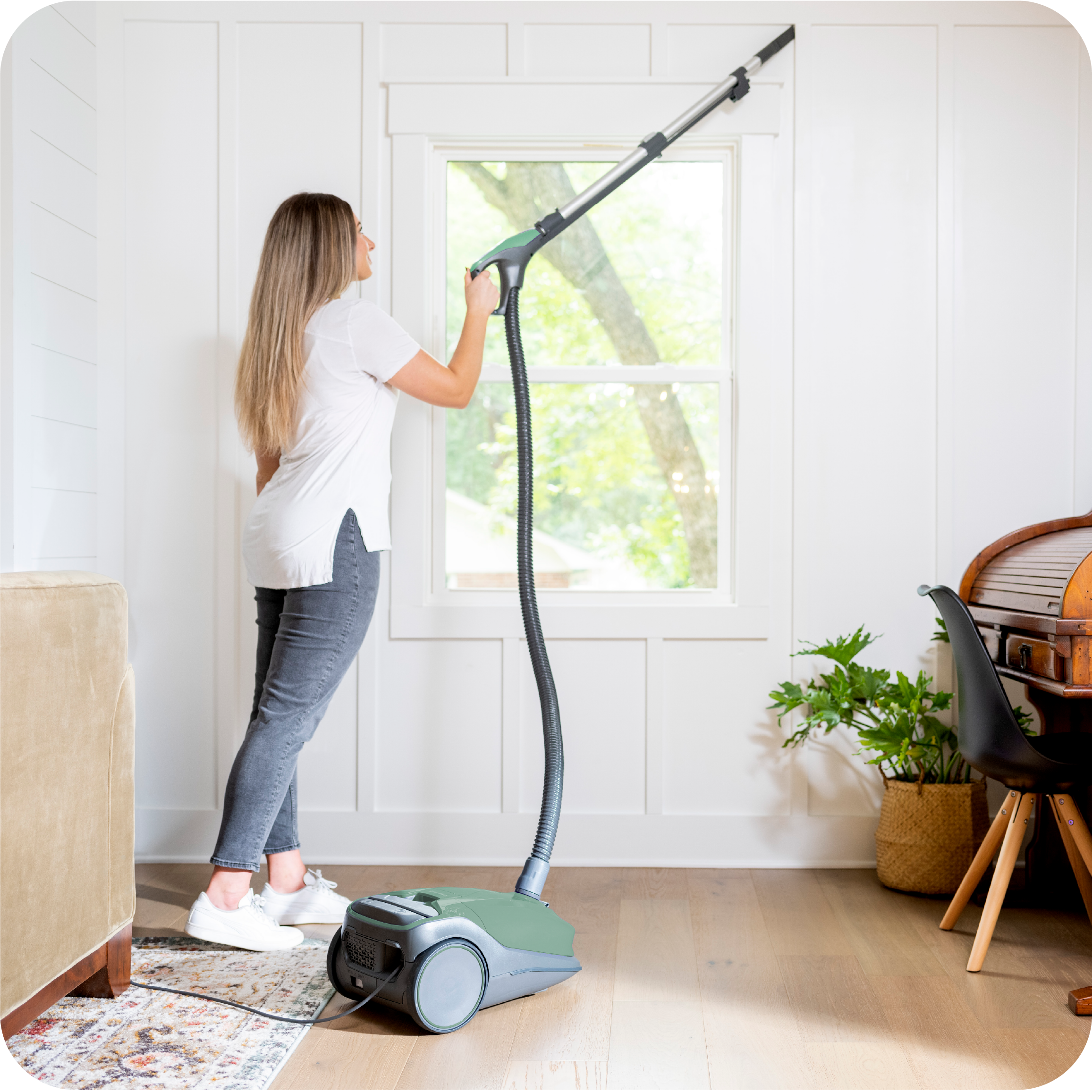 Person using a canister vacuum cleaner in a bright living room.