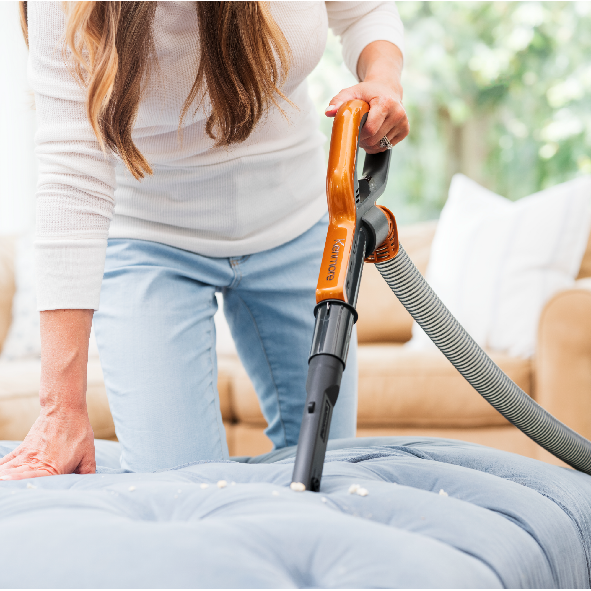 Person is shown vacuuming crumbs from upholstered furniture with handheld part of vacuum.