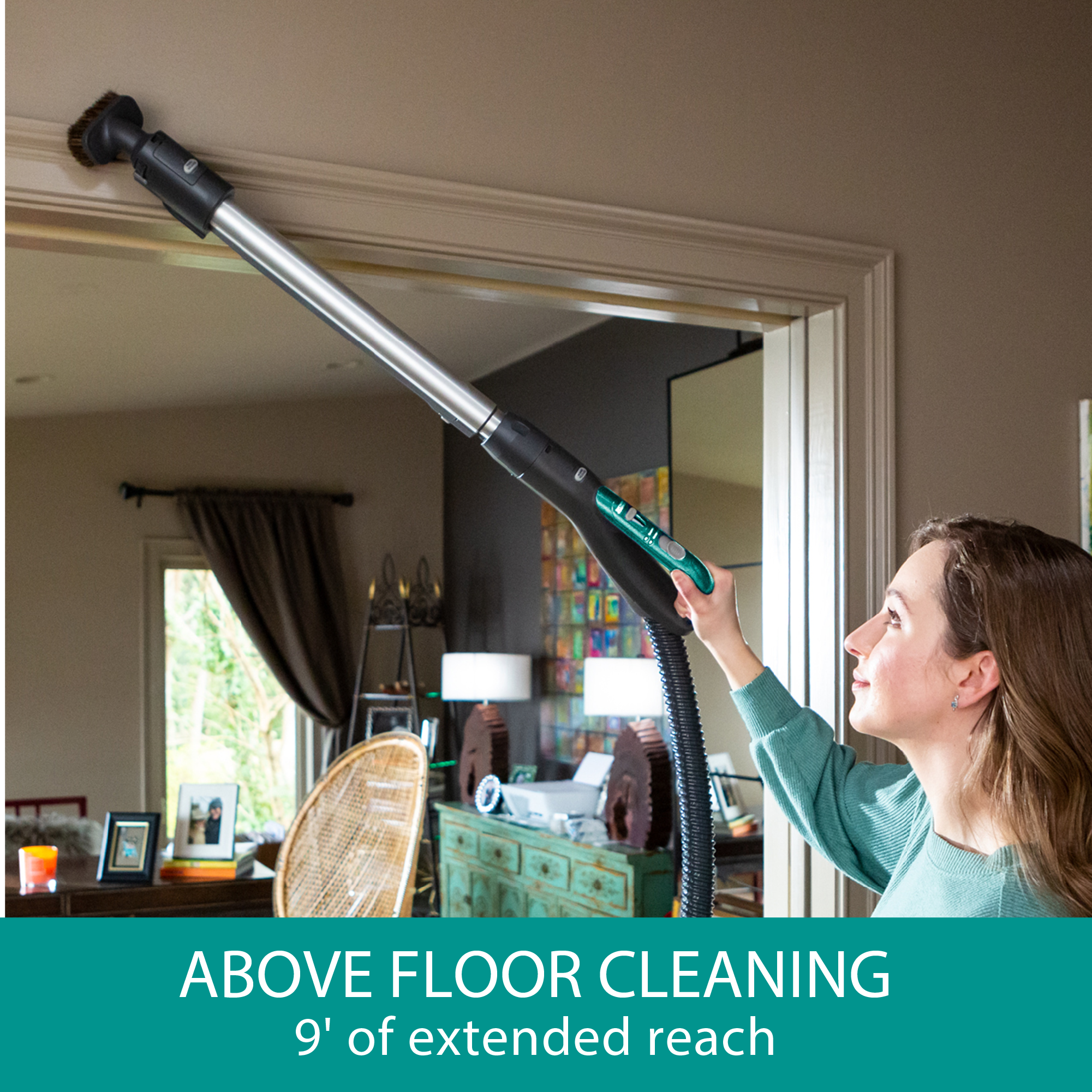 Person using a canister vacuum cleaner with an extended reach to clean above a door frame.