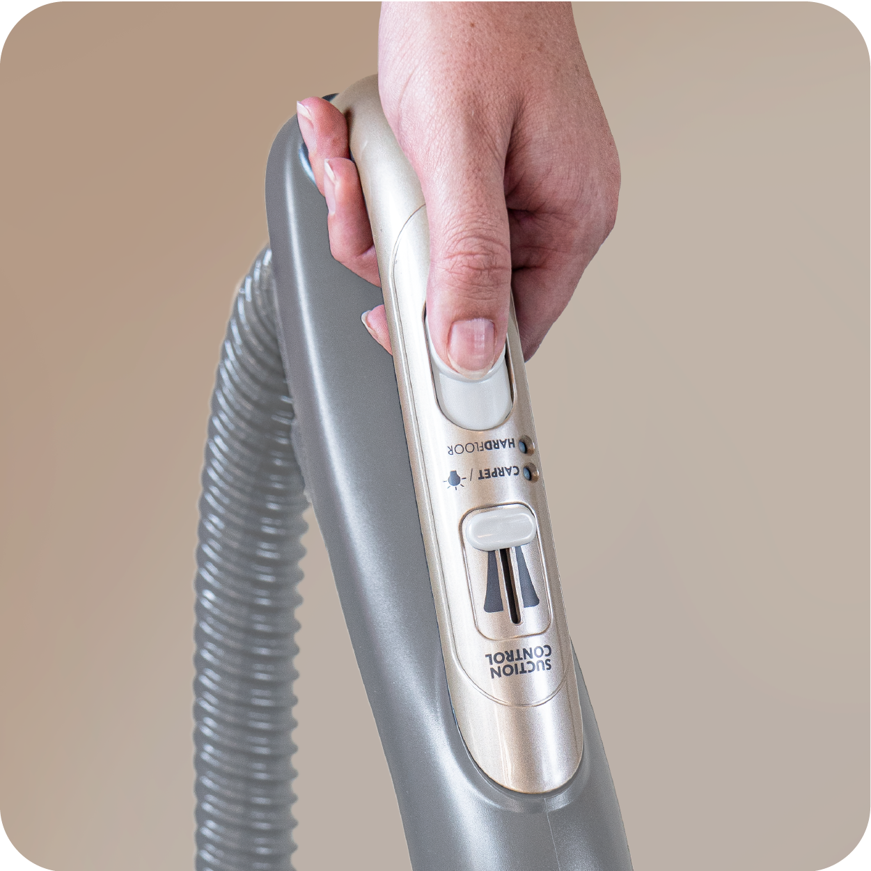 Hand holding a silver handheld vacuum cleaner on a beige background