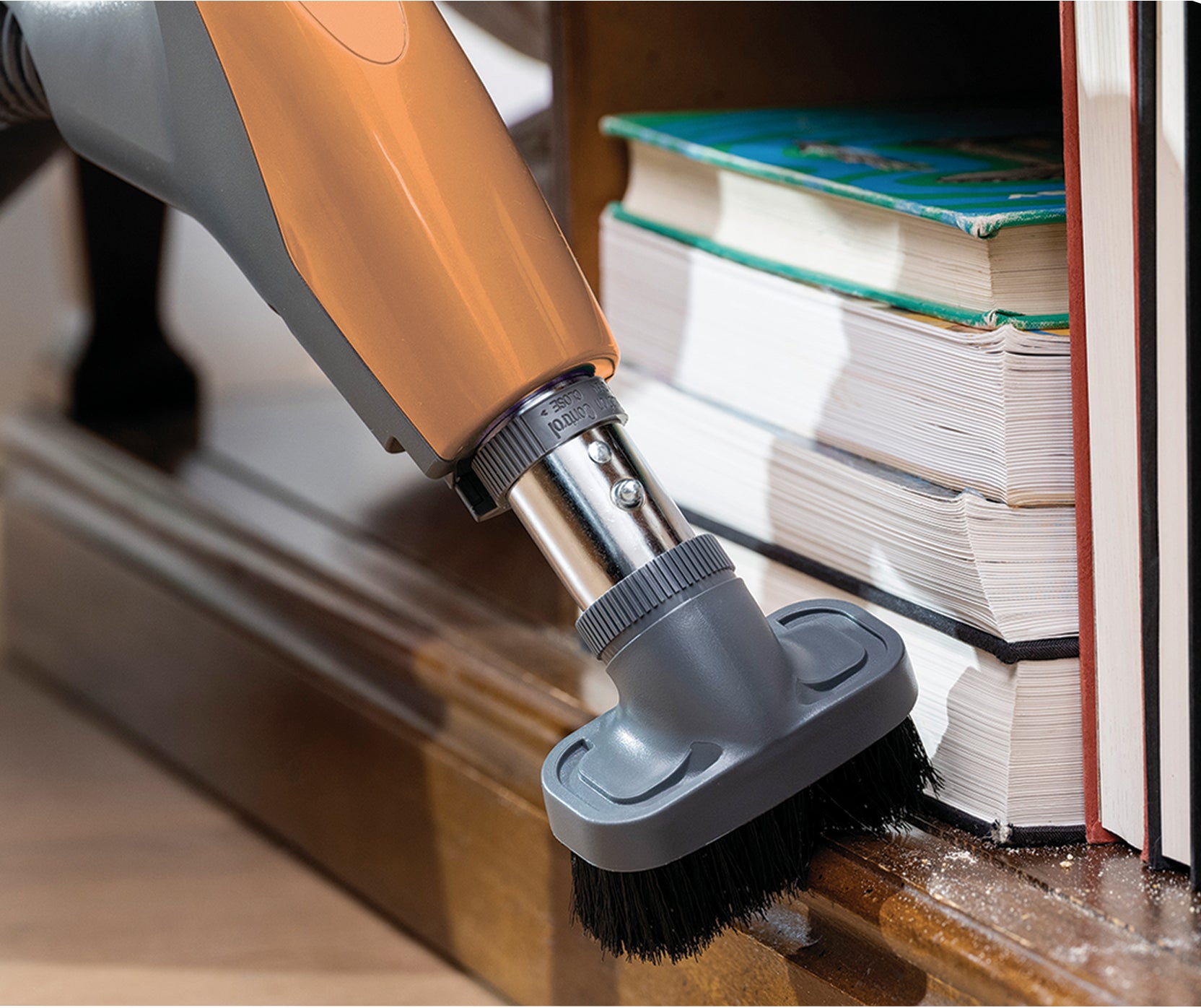 canister vacuum cleaner with dusting brush attachment cleaning a piece of furniture with books nearby