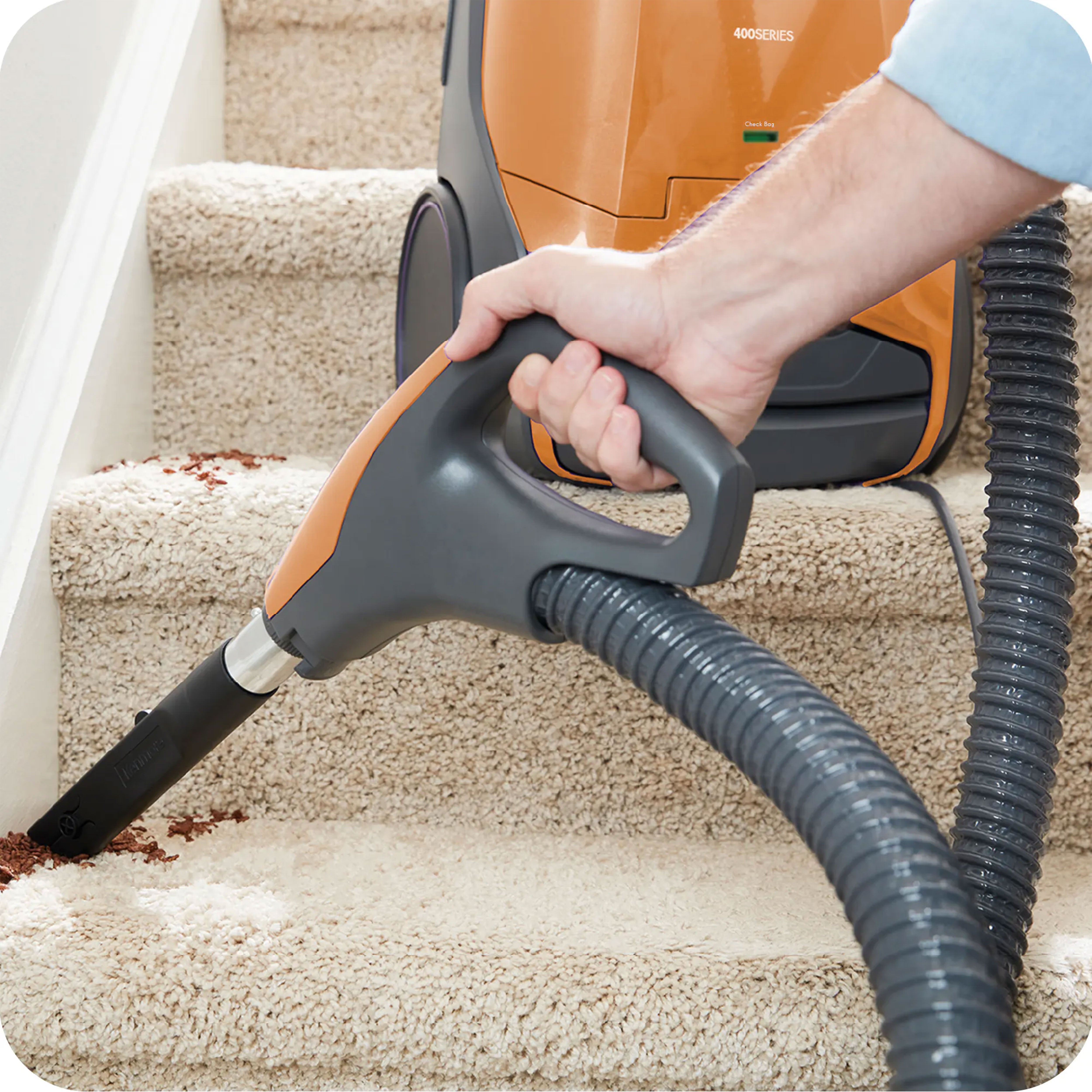 Person using a canister vacuum cleaner with crevice tool attached on a carpeted staircase