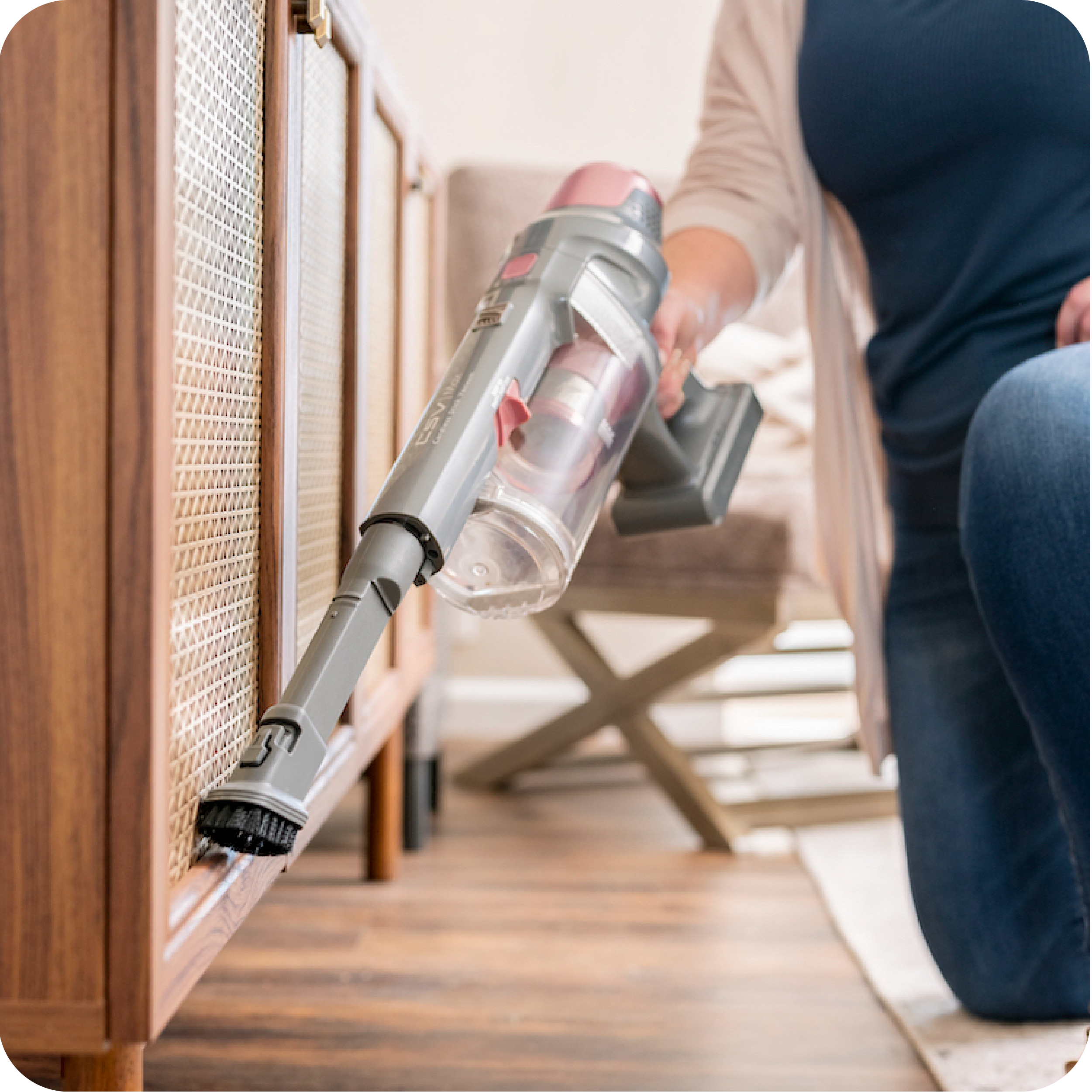 Person using a handheld vacuum cleaner to clean a wooden cabinet.