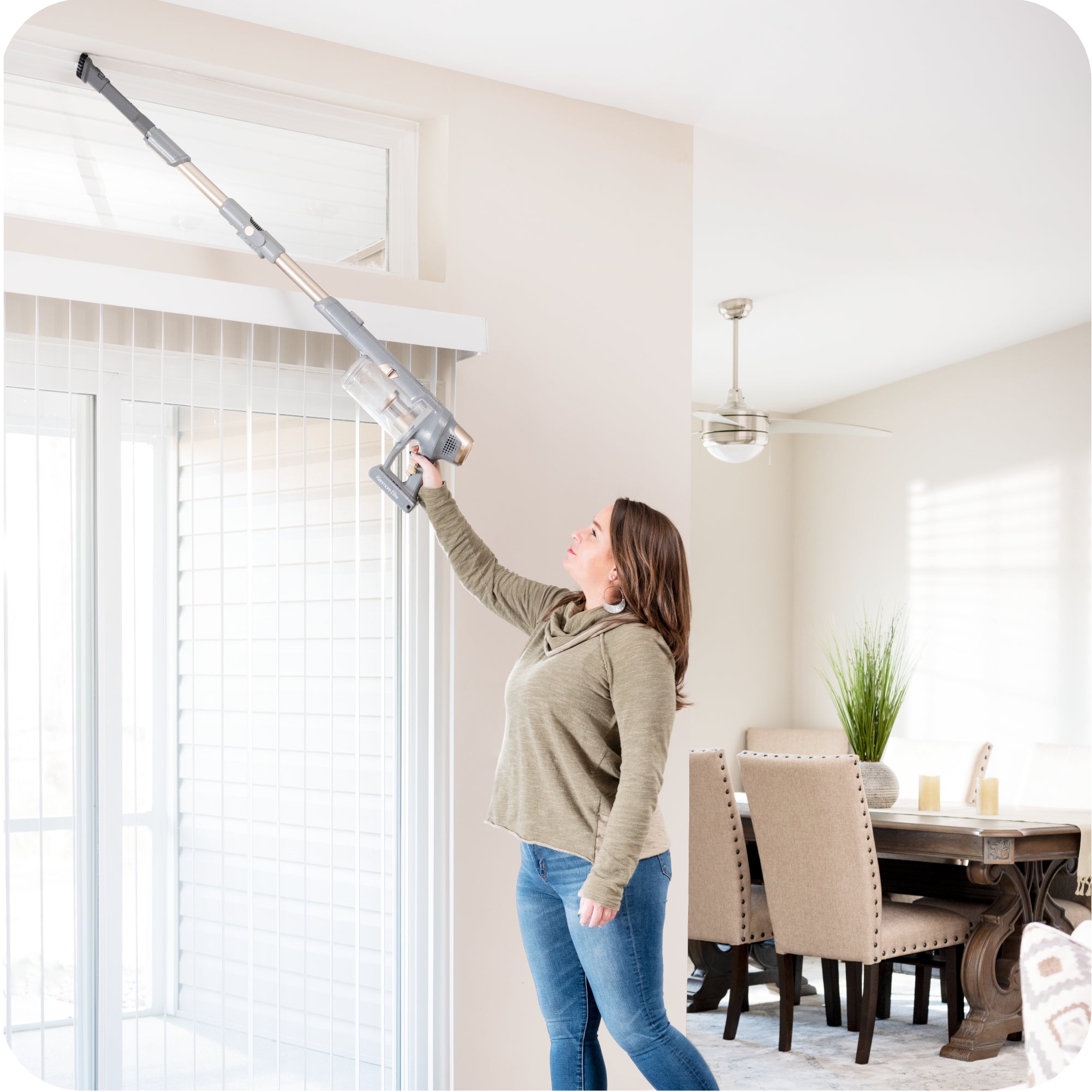 Person shown using long reach of stick vacuum to clean above a window.