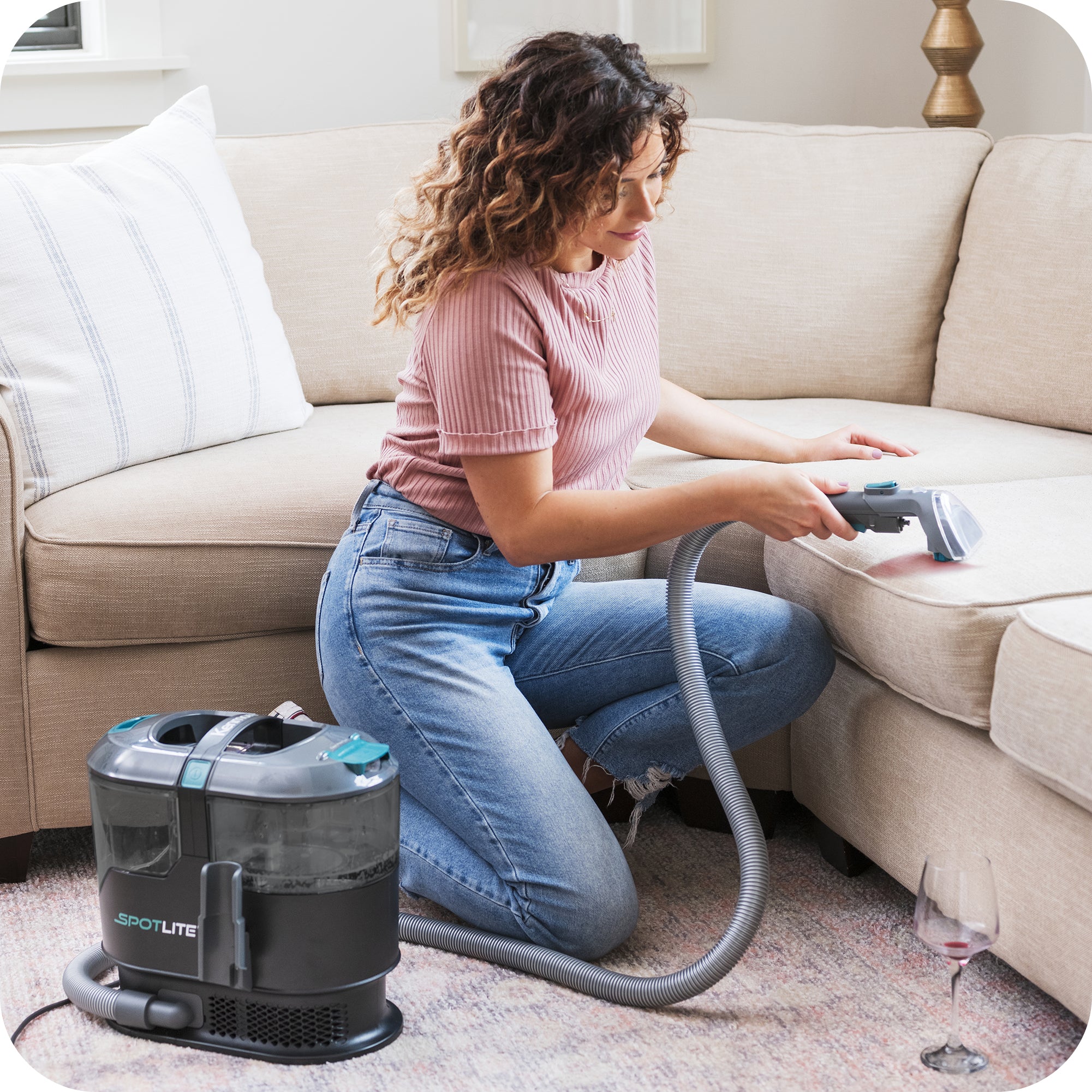Woman kneeling next to sofa cleaning stain with Kenmore SpotLite.