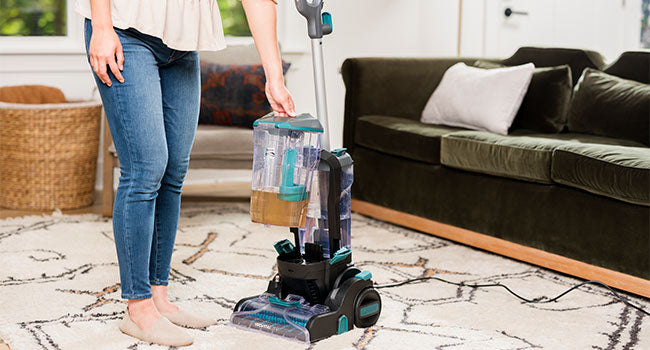 A person removes dirty water tank from machine  in a living room setting.