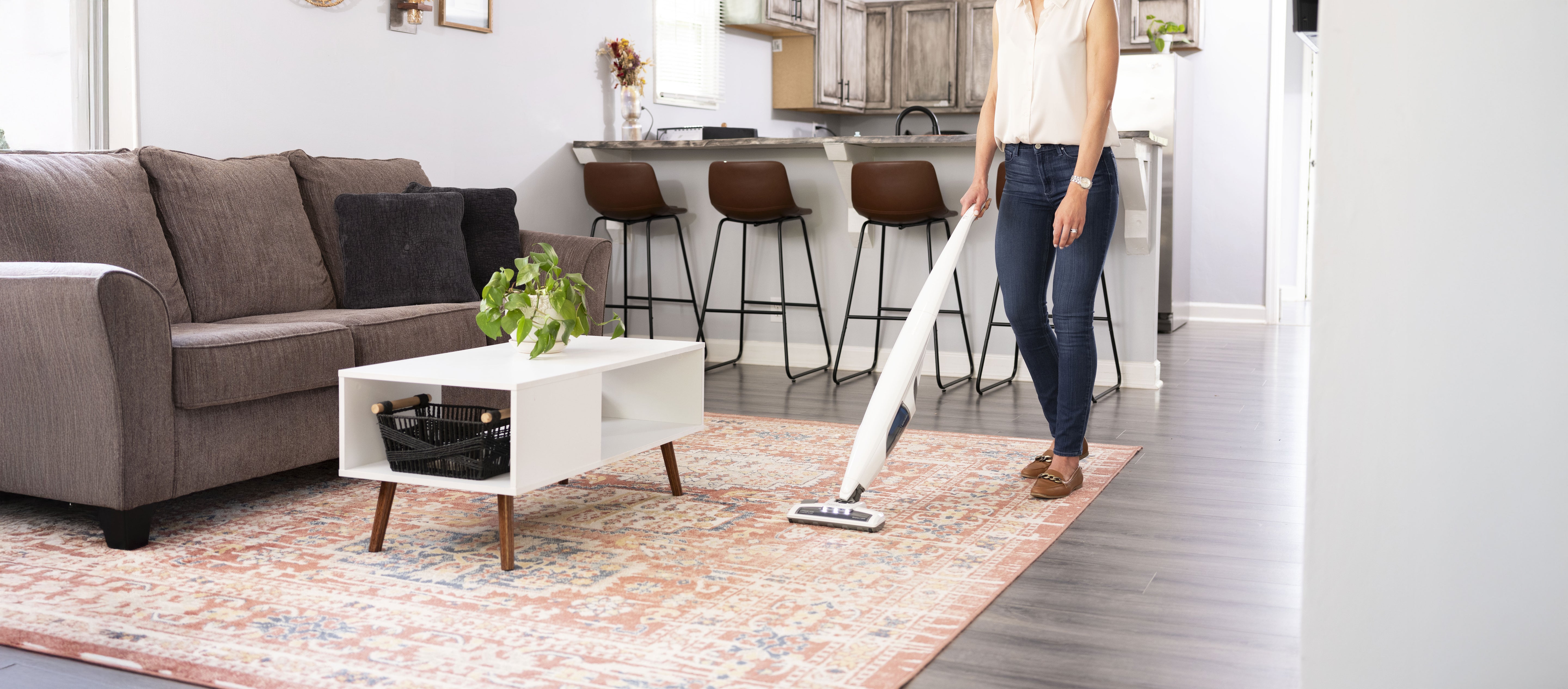 Person using a stick vacuum cleaner on a carpet in a living room.
