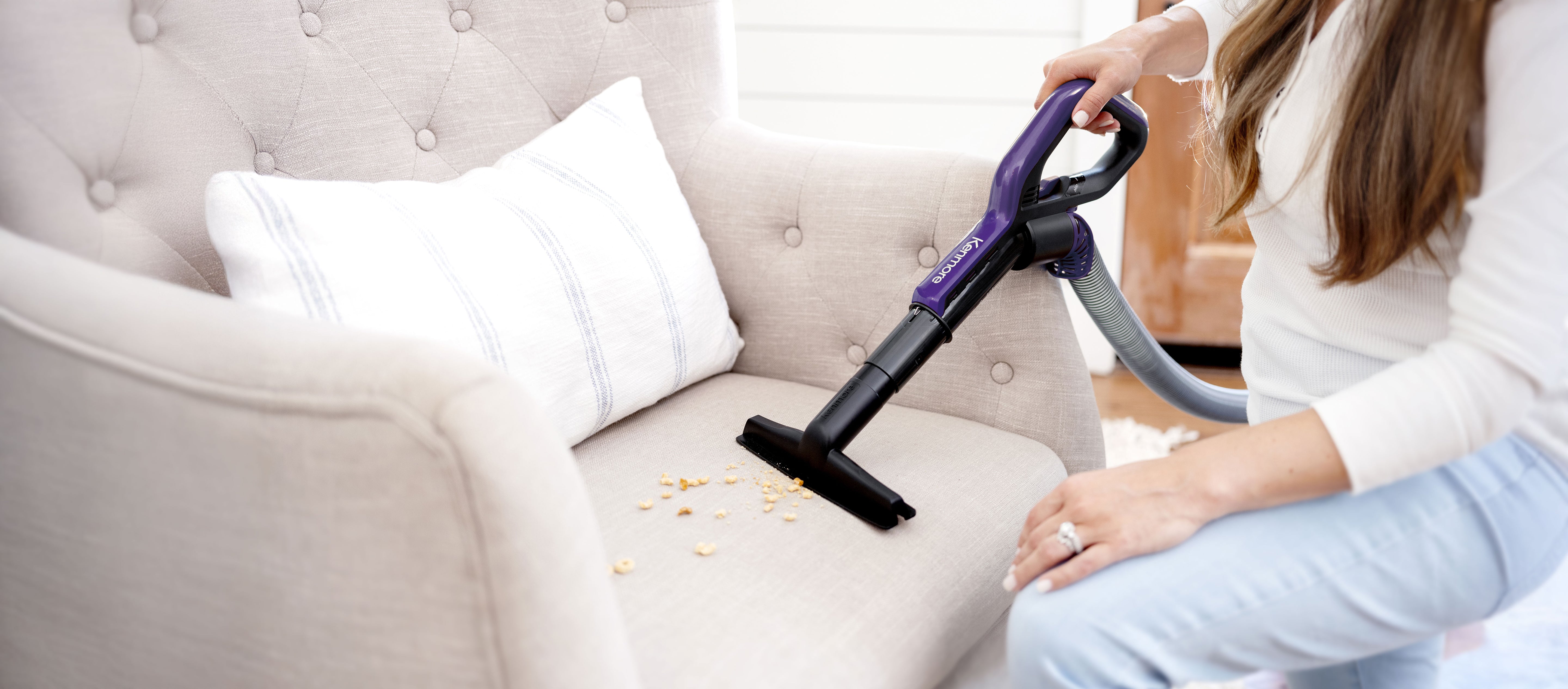 Person using an upholstery tool attachment from an upright vacuum cleaner on a sofa