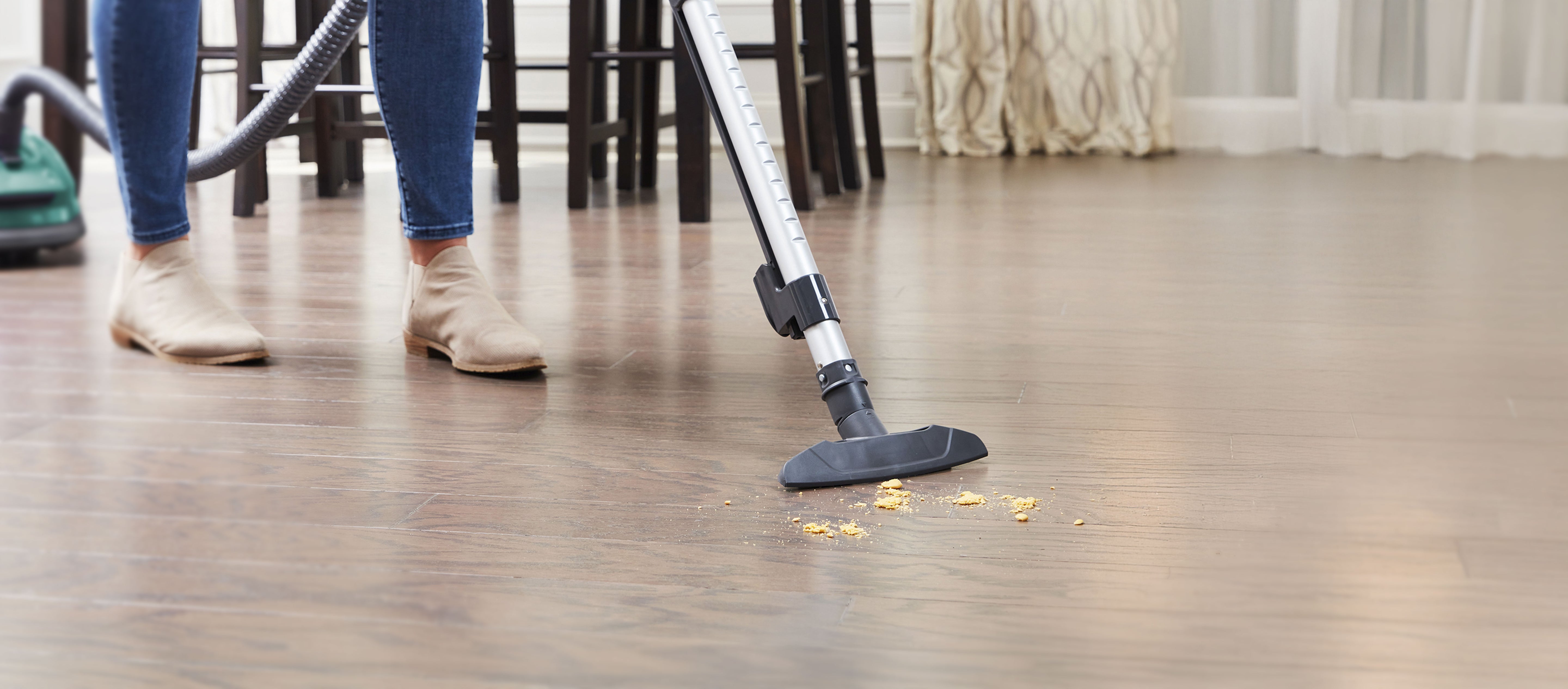 Person cleaning a wooden floor with a vacuum cleaner bare floor attachment.