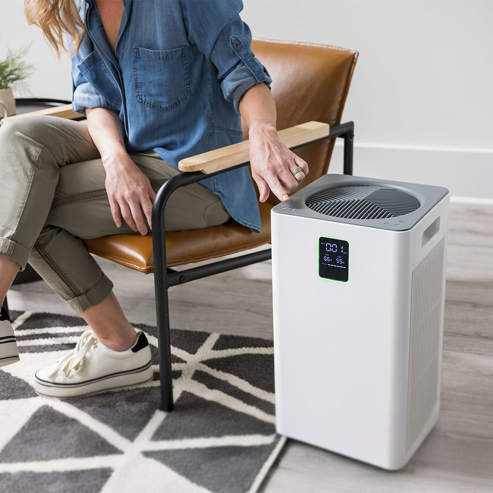 Person sitting on a chair next to an air purifier in a room.