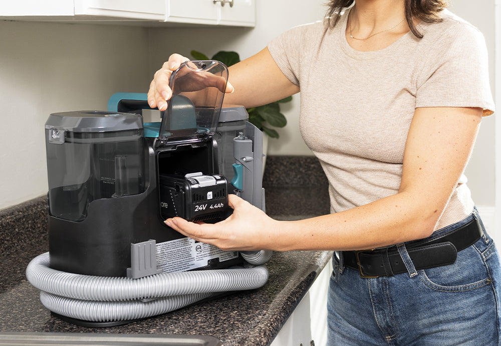Person inserting a battery into a spot carpet cleaner on a kitchen counter