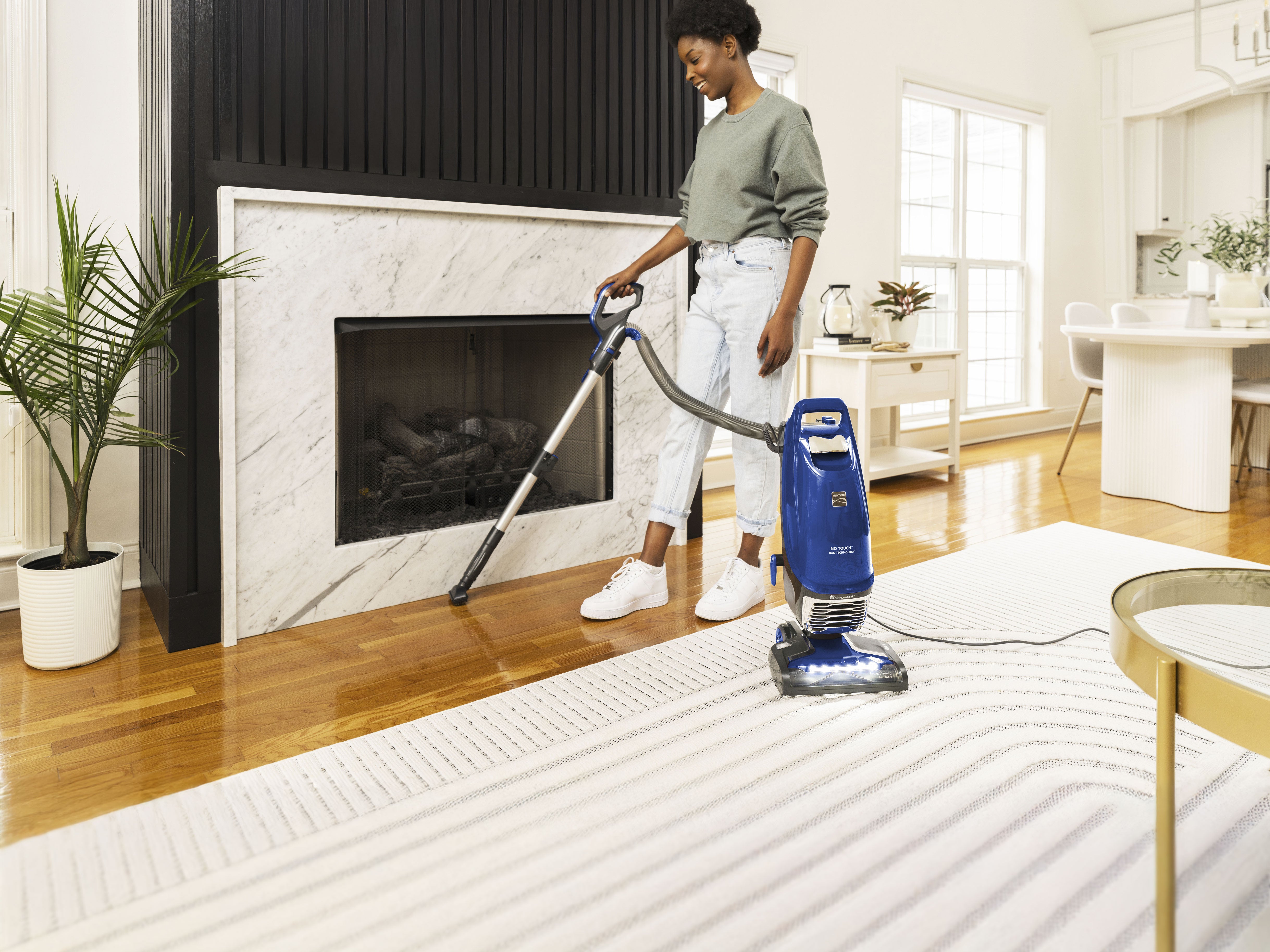 Person using a vacuum cleaner in a living room with a fireplace.