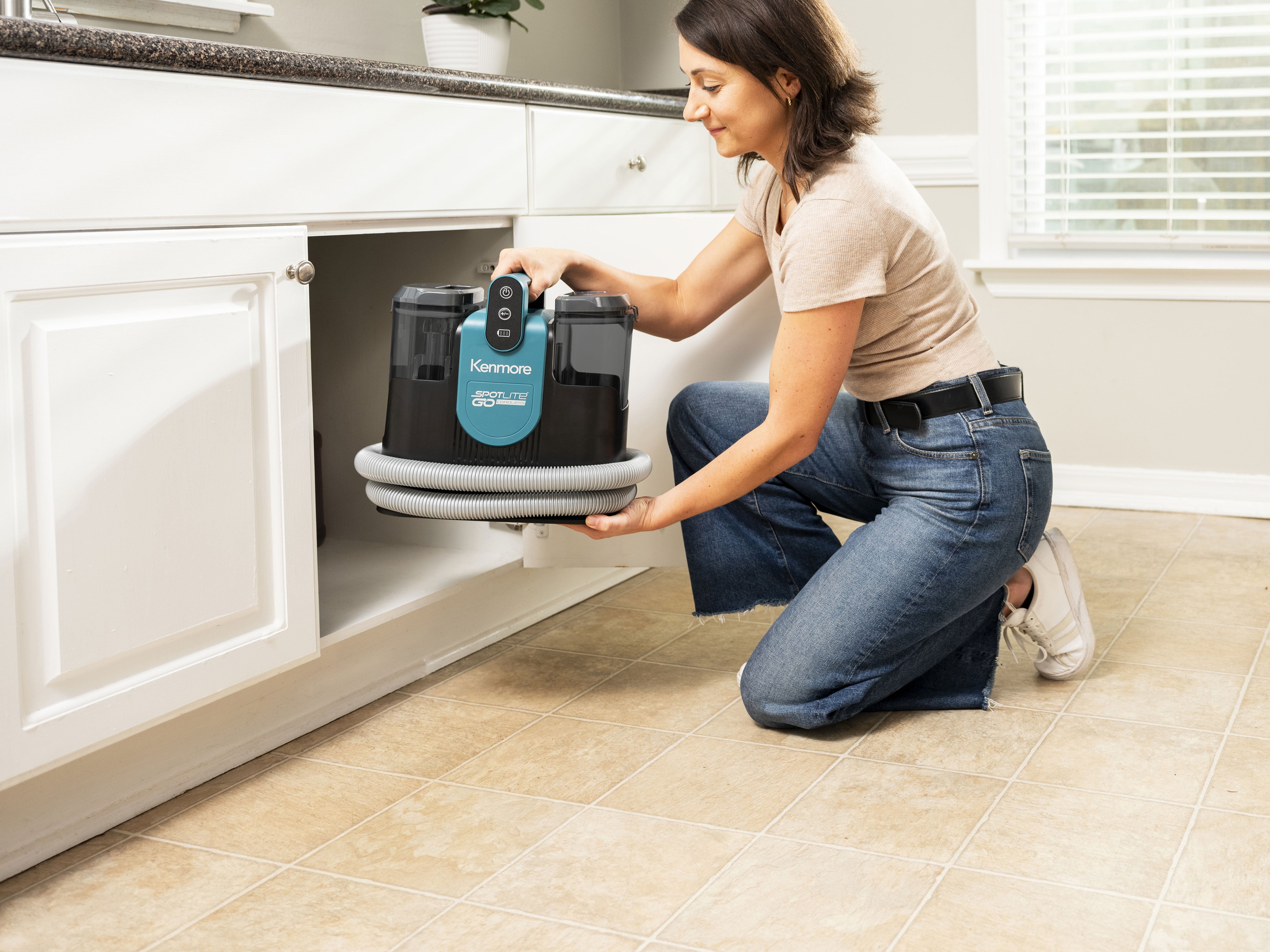 Person storing a portable spot carpet cleaner in a kitchen cabinet