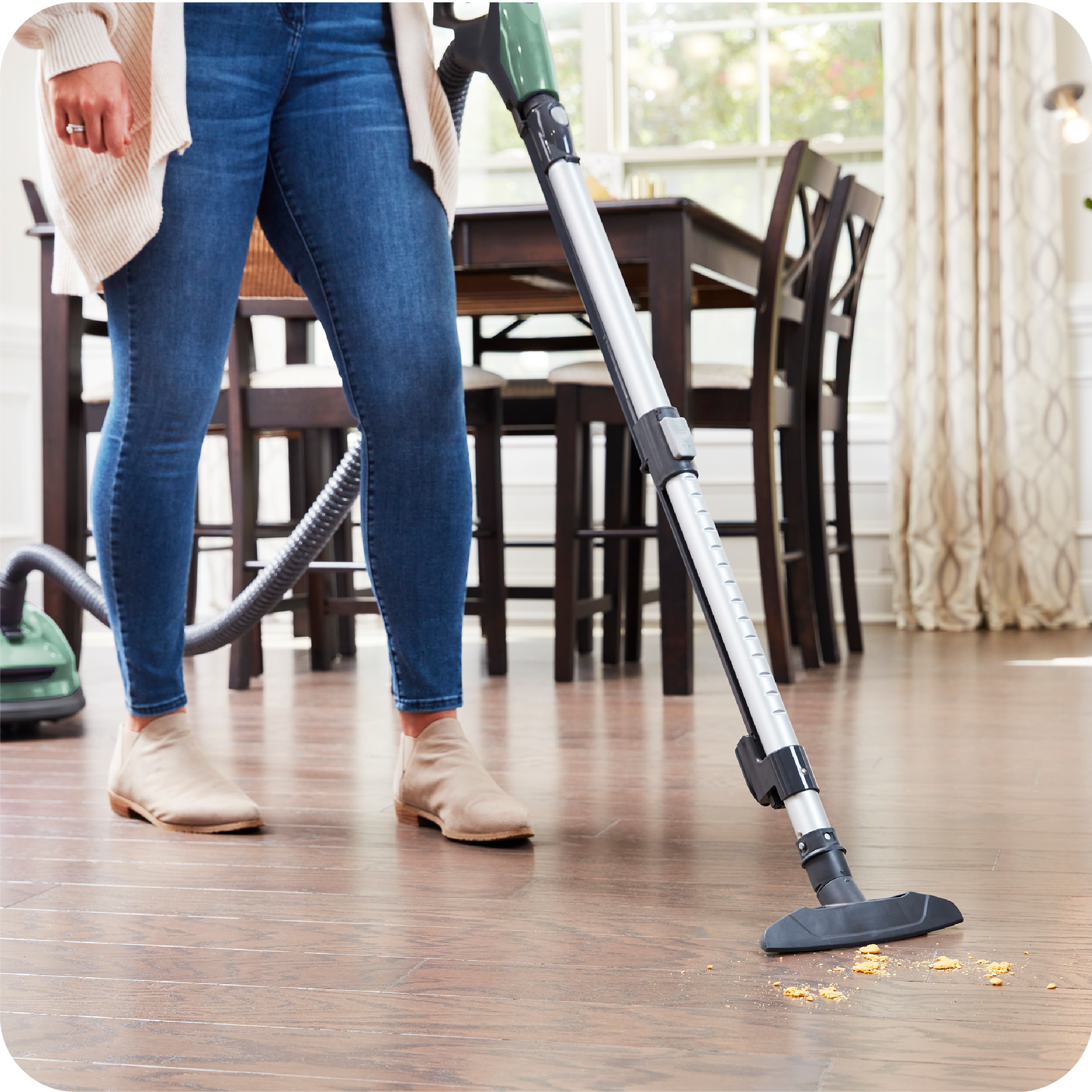 Person cleaning a wooden floor with a canister vacuum cleaner in a home setting.
