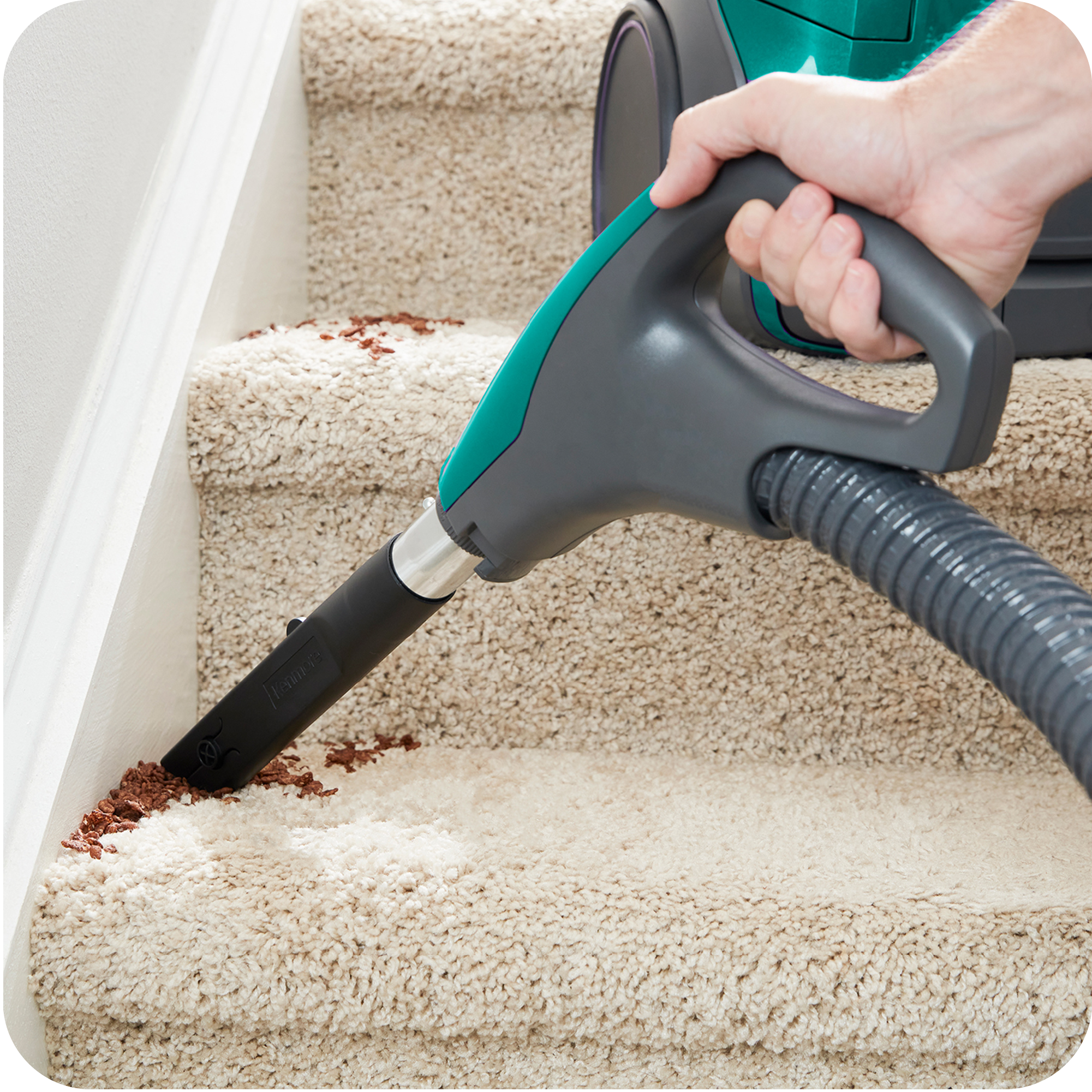 Person using a canister vacuum cleaner with crevice tool attached to clean a carpeted staircase.